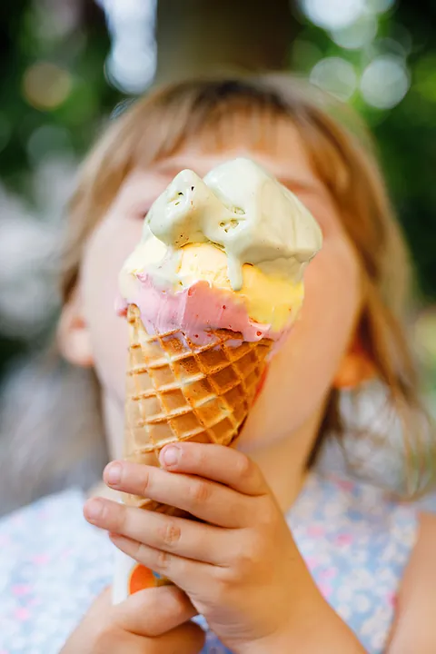 Mädchen hält Eistüte mit 3 Kugeln vors Gesicht